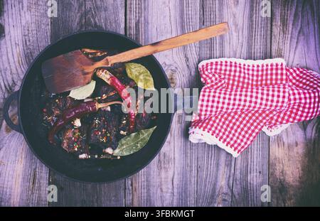 Cooked pork ribs on a black cast-iron frying pan with a handle, meat in spices and red chili pepper, top view, vintage toning Stock Photo