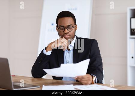 Pensive black manager sitting in office, reading papers Stock Photo