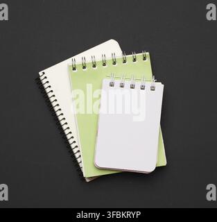 Stack of spiral open notebooks with blank white sheets on a black background, top view Stock Photo