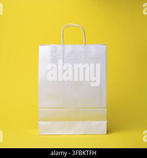 White paper disposable bag with handles on yellow background, zero waste Stock Photo