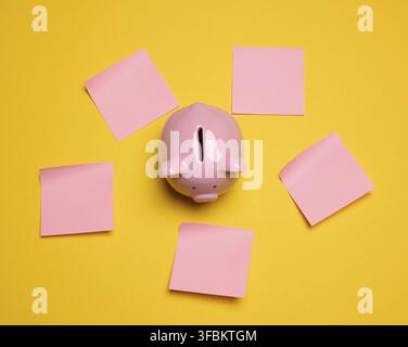 Pink ceramic piggy bank and paper stickers on a yellow background, top view Stock Photo