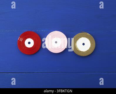 Twisted red, pink, golden silk ribbons on a blue background, element for the designer, top view Stock Photo