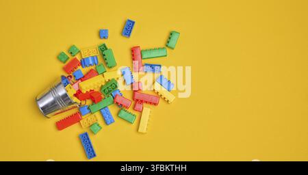 Vibrant colorful building bricks spilling from a silver metal bucket onto a yellow background. Play, fun, creativity, or construction concept Stock Photo