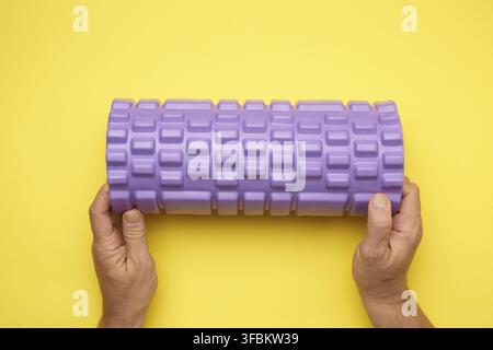 Two male hands hold purple massage roll for back and body on yellow background, top view Stock Photo