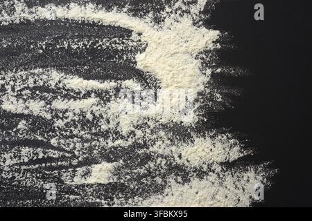White wheat flour scattered on a black wooden table, top view, kitchen backdrop Stock Photo