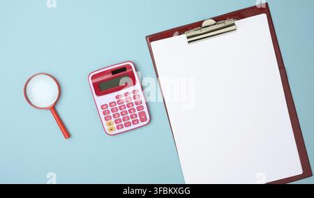 Pink calculator, folder with blank white sheets and black magnifier on a blue background, top view Stock Photo