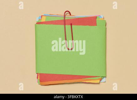 Stack of multi-colored sticky notes secured with a red paper clip, placed on a beige background. Top view Stock Photo