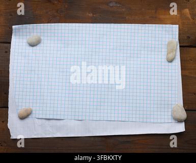 White sheet of paper in a cage on a brown wooden background, place for an inscription Stock Photo