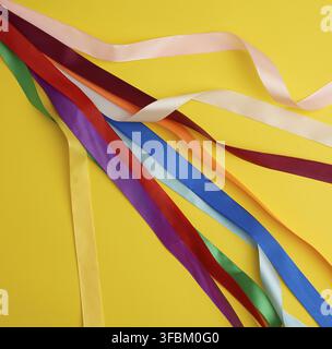 Many silk multi-colored ribbons on a yellow background, top view Stock Photo