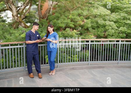 Asian male and female nurses using smartphones on balcony during breaktime Stock Photo