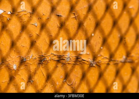 Close up view of chain link fence net shadow projected on an old yellow painted surface with cracked paint texture outdoors in bright sunlight. Stock Photo