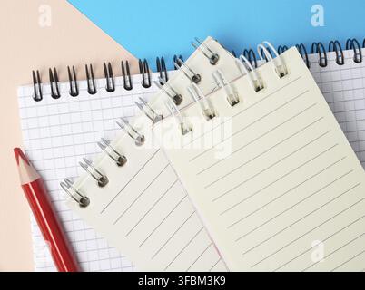 Red wooden pencil and stack of spiral open notebooks with blank white sheets on a blue background, top view Stock Photo
