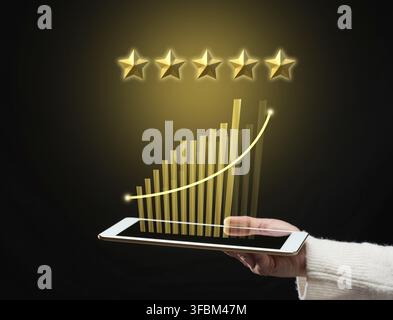 Female hand holds a tablet and five gold stars above it. App evaluation. User reviews, business rating Stock Photo