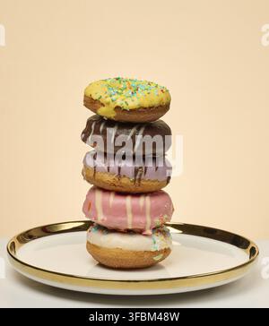 Stack of donuts with different toppings and glazes on round plate, beige background Stock Photo