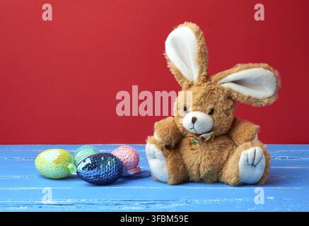 Cute rabbit toy and decorative Easter eggs with sequins on a red background, festive backdrop Stock Photo