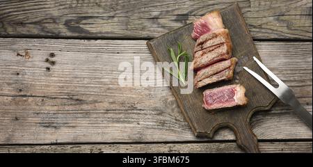 Sliced fried beef steak New York striploin on a wooden cutting board, degree of doneness rare, copy space Stock Photo