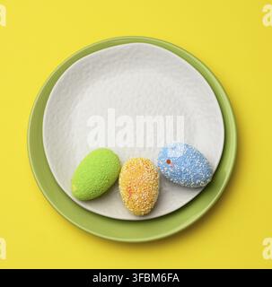 Decorative easter eggs in a round white ceramic plate on a yellow background, top view Stock Photo