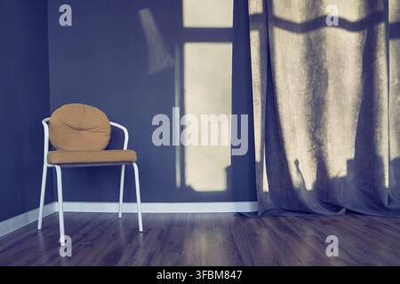 Dark blue room with modern chair, metal frame with soft brown seat, curtains, window shadow, brown wooden floor. Background with copy space, empty. Te Stock Photo