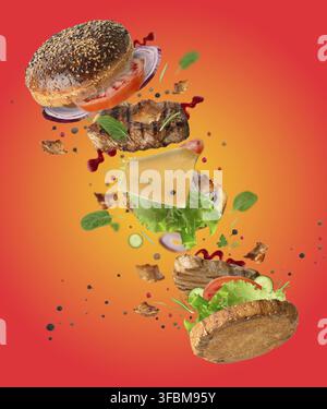 Delicious burger with flying ingredients, pieces of vegetables, spices and meat fried steak on orange background Stock Photo