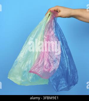 Hand holds empty multi-colored plastic bags on a blue background, concept of rejection of plastic and the transition to eco-packaging Stock Photo