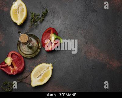 Red bell pepper halves, lemon, thyme sprigs, and a glass decanter of olive oil on a dark textured background. Top view, space for text Stock Photo