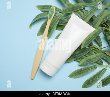 White plastic tube and bamboo toothbrush on blue background, top view Stock Photo
