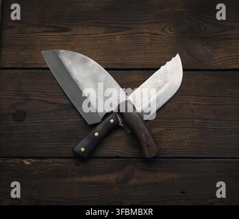 Metal sharp kitchen knives in a wooden handle on a brown table made of boards, top view Stock Photo