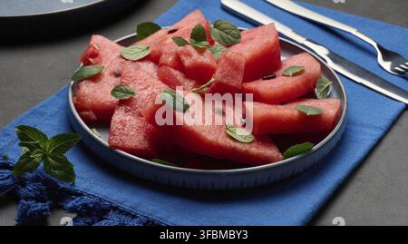 A plate of sliced ??watermelon garnished with fresh mint leaves. A plate of fresh, summery dessert sits on the table Stock Photo