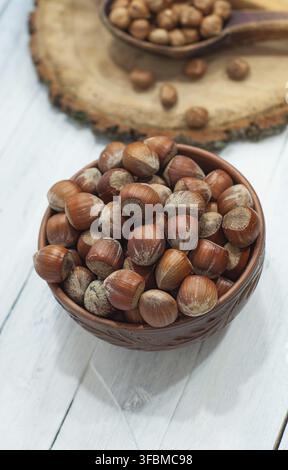 Nuts hazelnuts in the shell in brown clay bowl on a white wooden surface, top view Stock Photo