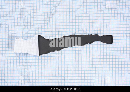 Texture of crumpled white paper in a cage, blue lines, torn edges on a black background Stock Photo