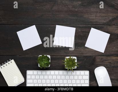 White wireless keyboard and mouse on a wooden brown table, next to three blank white sheets of paper, top view, copy space Stock Photo