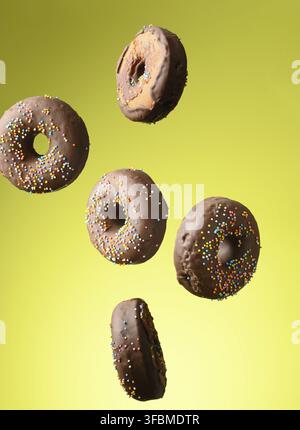 Chocolate round donuts with multicolored sugar sprinkles levitate on a green background Stock Photo