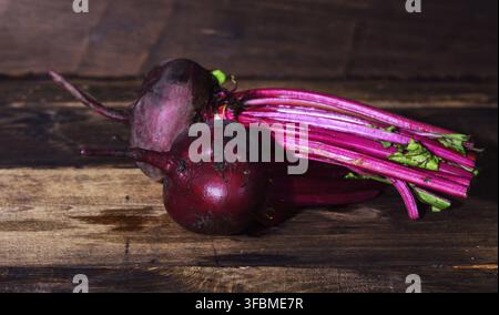 Two whole fresh beets with a tops on a brown wooden table Stock Photo