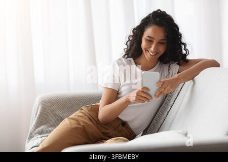 Happy woman using mobile phone at home Stock Photo