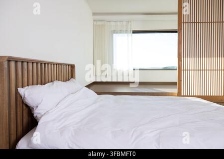 Unmade white bed with rumpled duvet and pillows in a bright modern bedroom with nobody present. Stock Photo