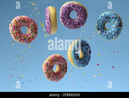 Sweet multicolored donuts levitate on a blue background, sugar sprinkles are flying around Stock Photo