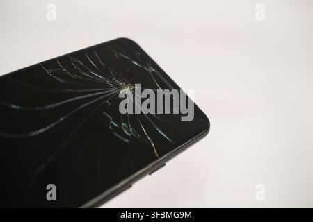 Black smartphone with a shattered cracked screen lying on a clean white surface, showing accidental device damage and repair needs. Stock Photo