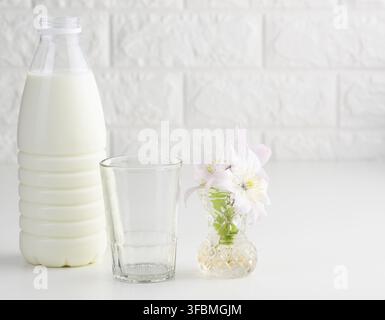 Plastic bottle with milk and empty glass cup on a white table. Breakfast Stock Photo