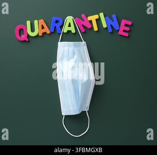 Inscription quarantine from multi-colored plastic letter on a green chalk board, hanging disposable medical mask Stock Photo