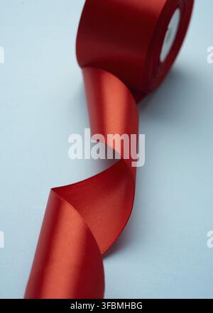 Curled red silk ribbon on blue background, close up Stock Photo