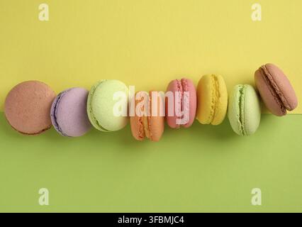 Baked multi-colored macaroon cookies lie in a row on a yellow-green background, overhead view Stock Photo
