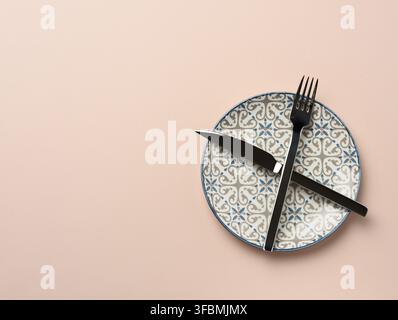 Round ceramic plate and crossed knife and fork on beige background, top view Stock Photo
