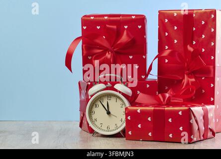 Alarm clock and stack of red gift boxes on blue background Stock Photo