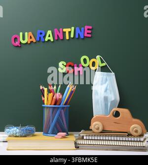 Inscription quarantine from multi-colored plastic letter on a green chalk board, hanging disposable medical mask Stock Photo