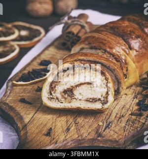 Baked roll with cinnamon and nuts on a wooden board, close up Stock Photo