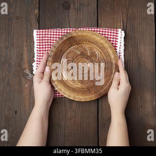 Two female hands holding an empty round wooden plate, top view Stock Photo