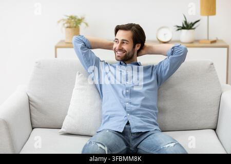 Relaxed Guy Sitting Holding Hands Behind Head On Sofa Indoor Stock Photo