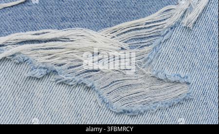 Fragment of blue jeans fabric with a hole, full frame, close up Stock Photo