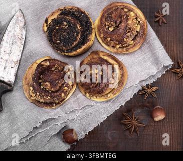 Round buns with cinnamon and poppies on a gray textile napkin, brown wood background, and top view Stock Photo