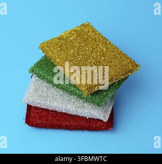 Stack of new multi-colored kitchen sponges for washing dishes on a blue background, close up Stock Photo